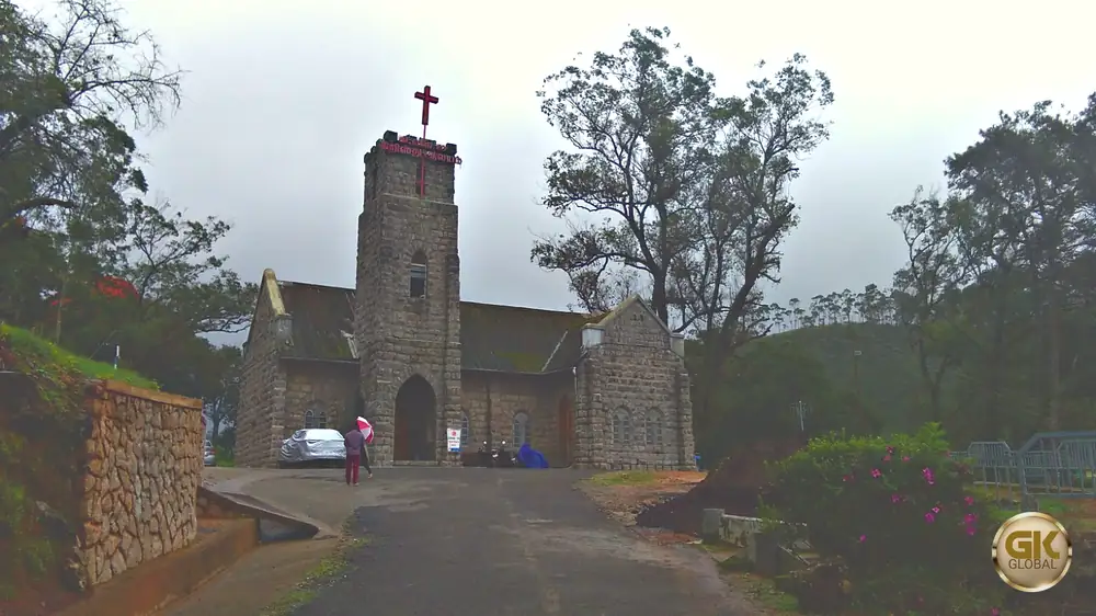 CSI Christ Church in Old Munnar, a granite Gothic church with a square bell tower topped by a red cross, among tall trees on a misty monsoon day